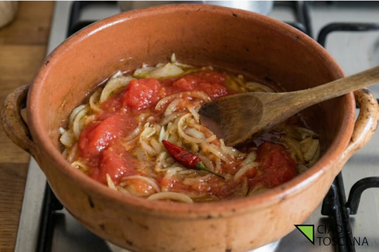 Aggiunta dei pomodori pelati al soffritto di cipolle nel tegame per preparare il sugo dell'Acquacotta Aggiunta dei pomodori pelati al soffritto di cipolle nel tegame per preparare il sugo dell'Acquacotta